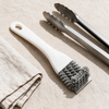 V-shaped grill brush laid out with barbecue tongs and a cloth