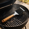 Grill brush resting on barbecue grates, half the grate scrubbed clean