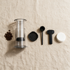Portable coffee press disassembled into its parts with whole coffee beans alongside