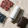 Compact Food Vacuum Sealer on linen beside sealed bags of steak, blueberries and coffee beans